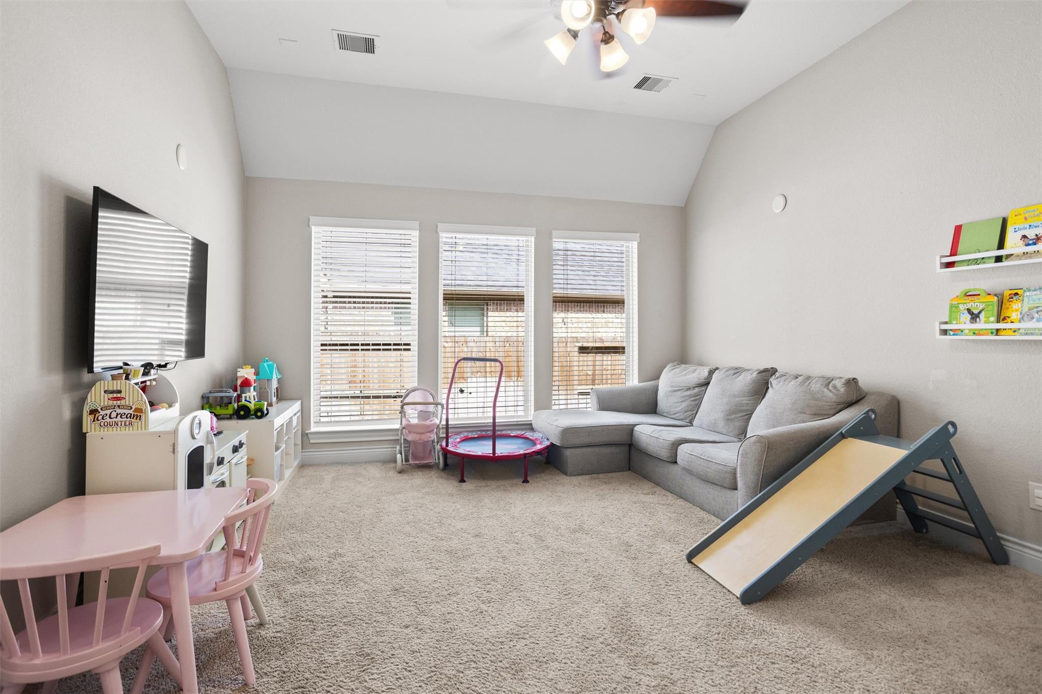 Furnished playroom with a gray sectional, children's toys, pink table, and indoor slide.