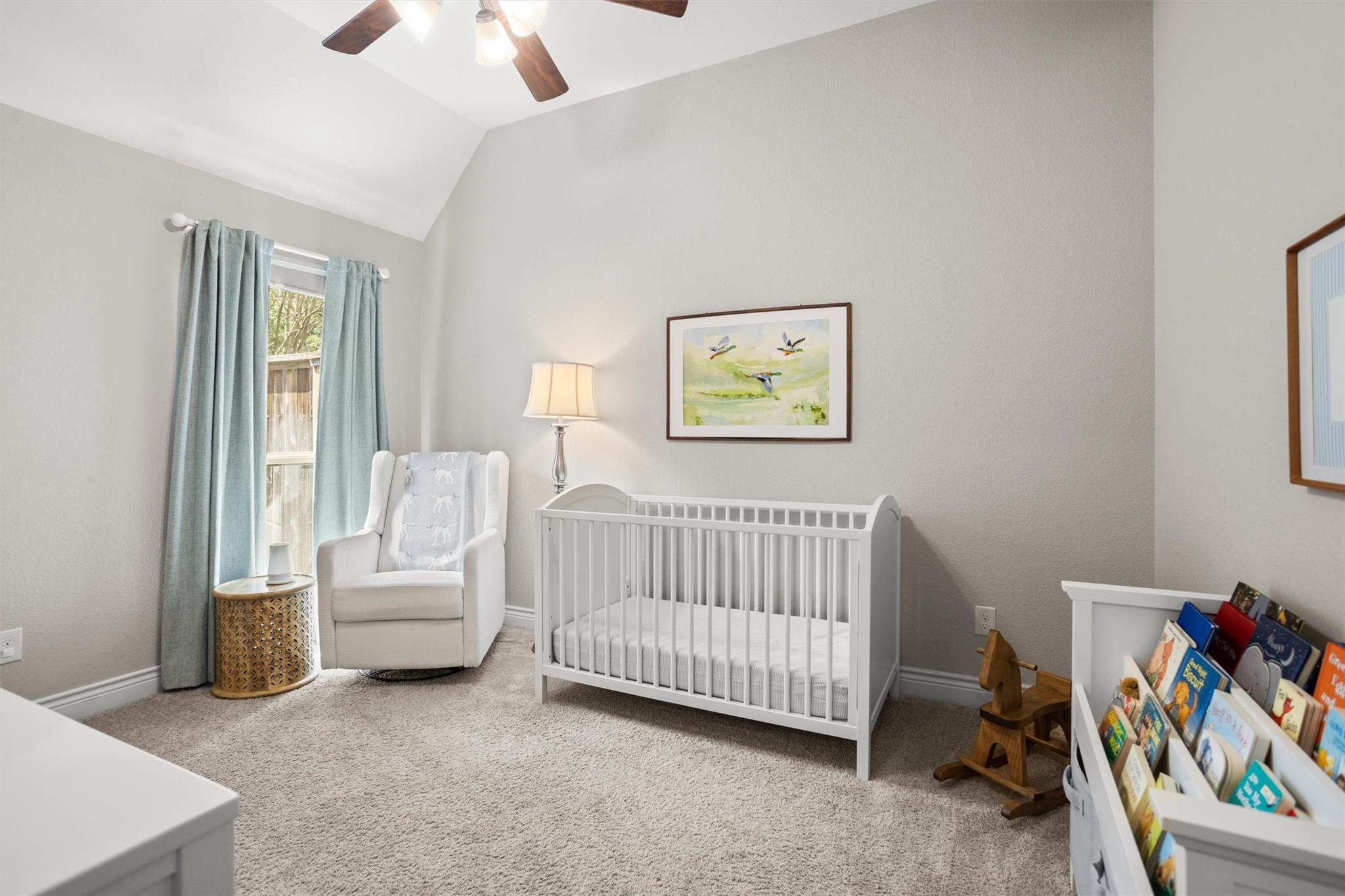 Nursery with a white crib, upholstered glider, and children's books beneath a vaulted ceiling.