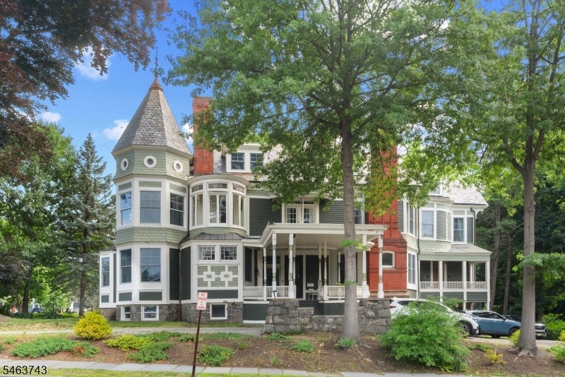 Large house with a conical turret, red brick accents, and a broad covered porch beneath mature trees.