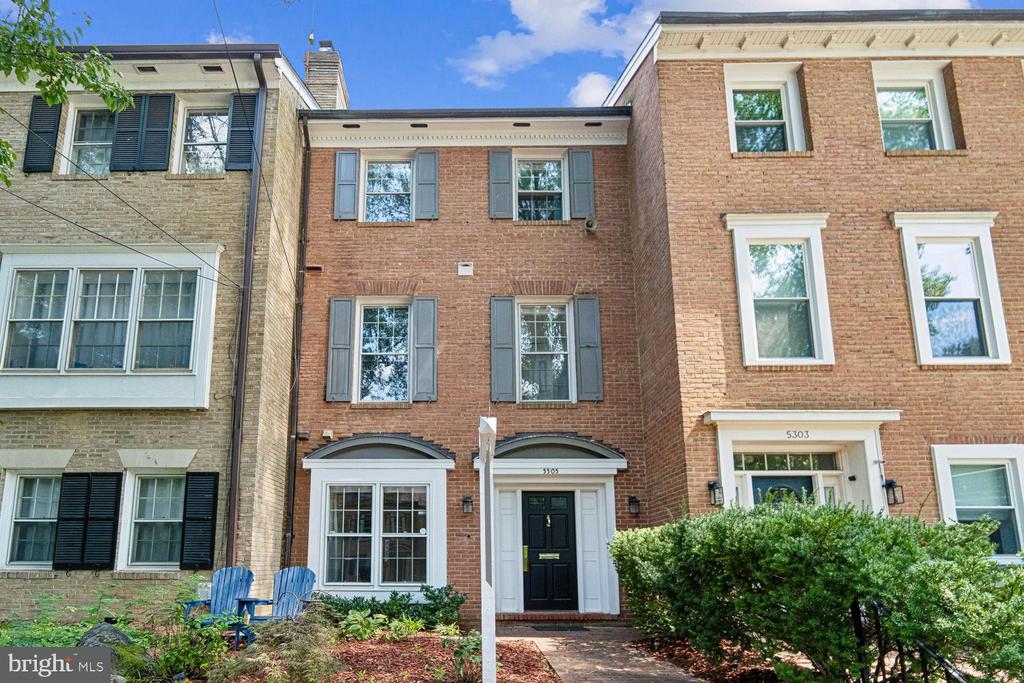 Red-brick townhouse with gray shutters, a black front door, and a landscaped entry path.