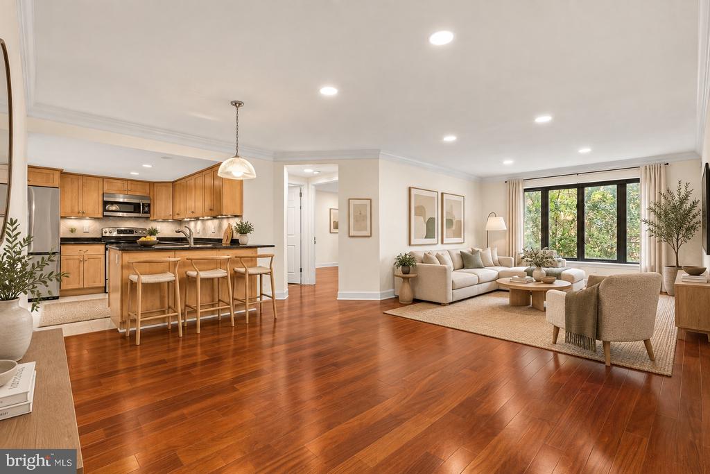 Open-plan kitchen and living room with warm wood cabinets, hardwood floors, and a large window overlooking greenery.