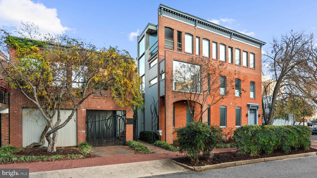 Multi-story red-brick residence with tall windows and a gated driveway along a tree-lined street.