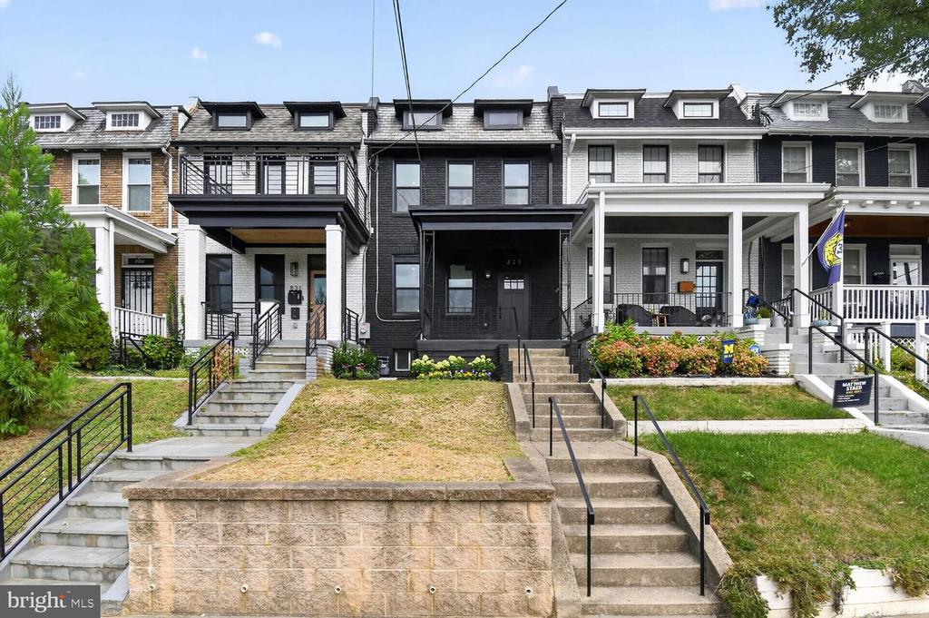 Dark brick row house centered between neighboring homes, with broad concrete steps and black railings.
