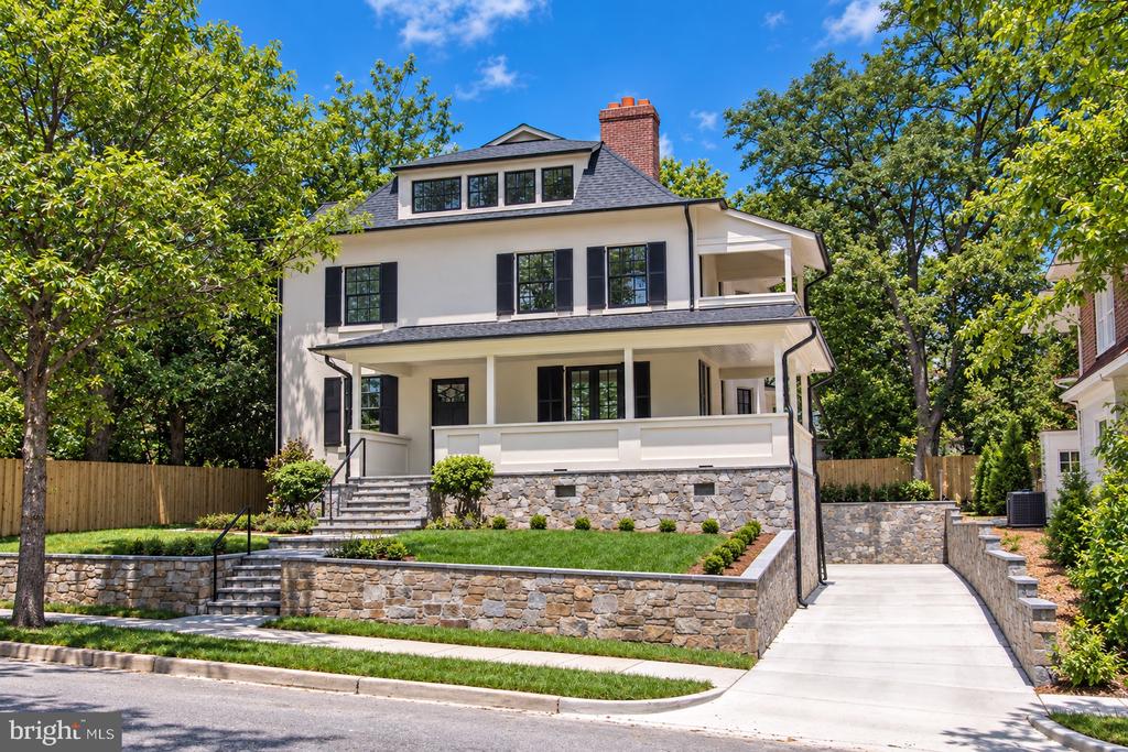 White two-story house with black shutters, a broad covered porch, stone retaining walls, and a long driveway.