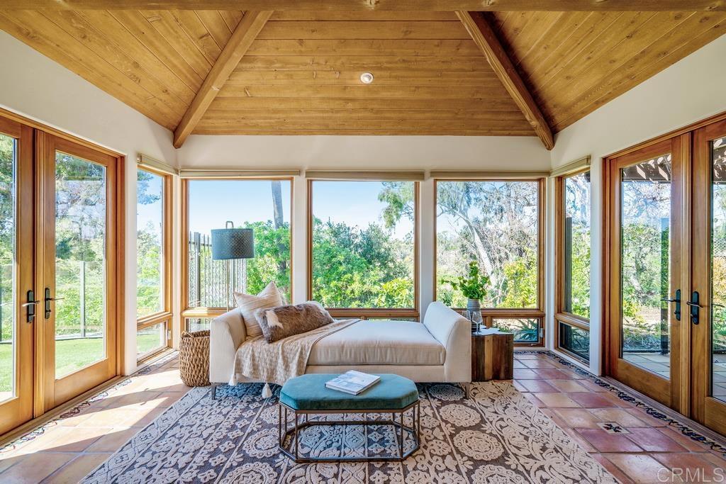 Sunroom with a vaulted wood ceiling, large garden-facing windows, cream sofa, and patterned rug.
