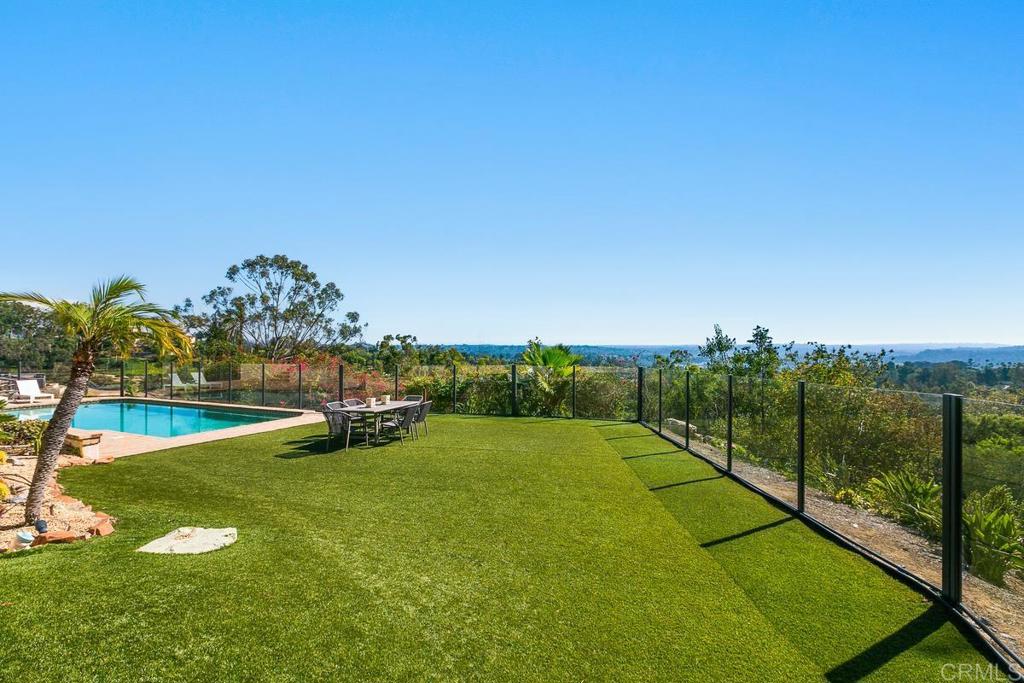 Backyard pool and lawn with glass fencing and a distant wooded view.