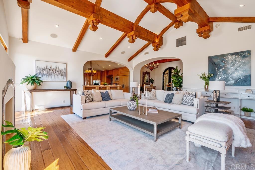 Living room with exposed timber ceiling beams, white sofas, and arched openings to the kitchen.