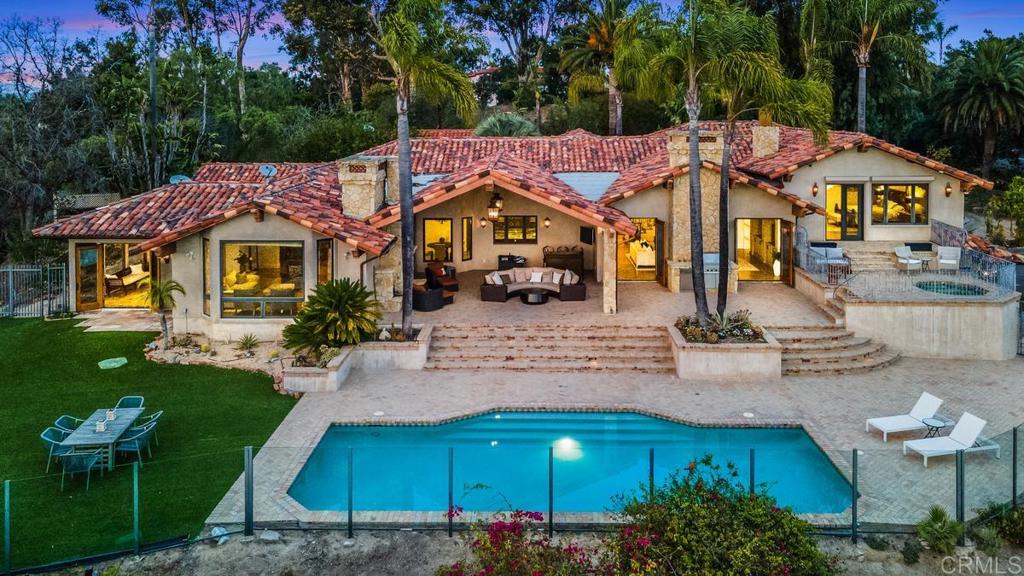 Rancho Santa Fe home with a red tile roof, covered patio, and swimming pool at dusk.