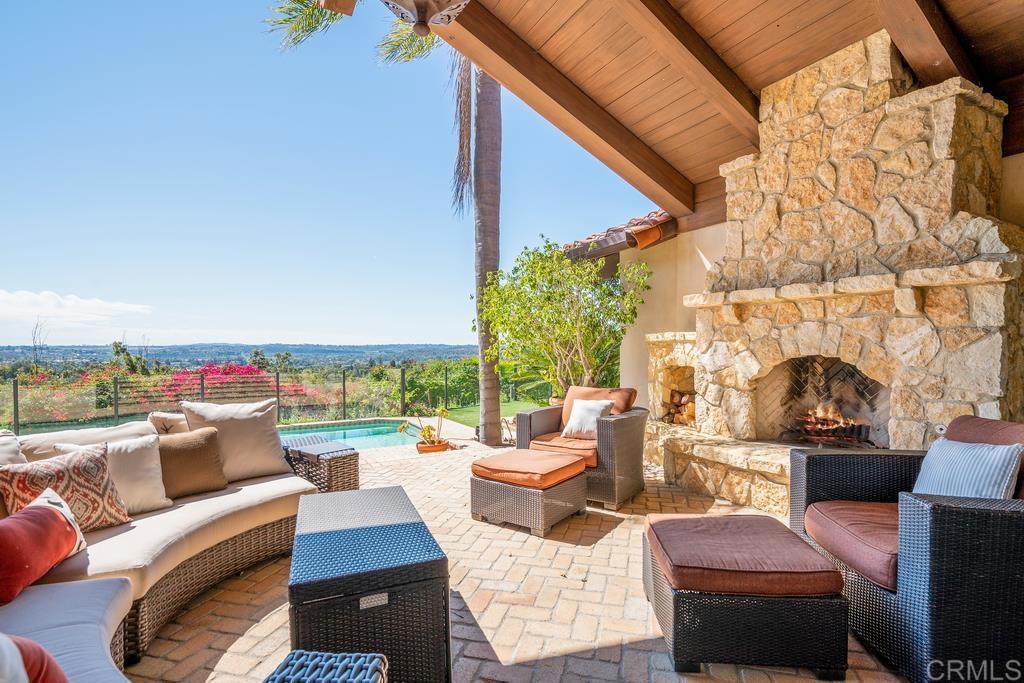 Covered patio with wicker seating and a stone fireplace overlooking a pool and valley.