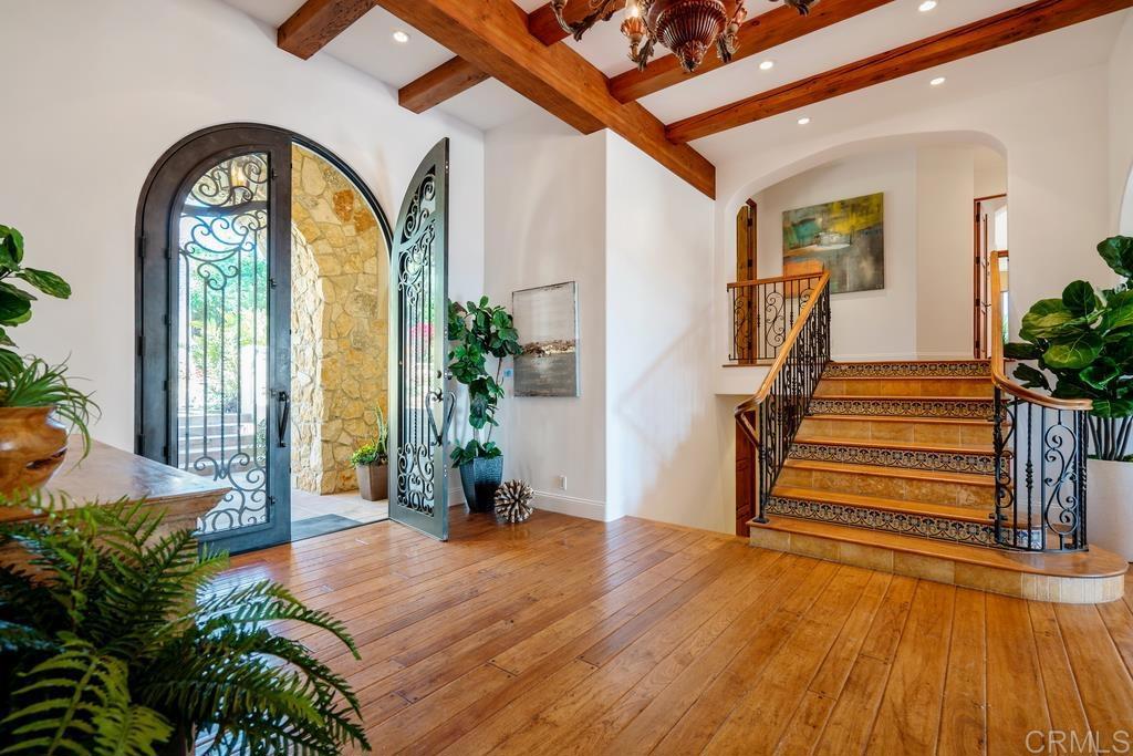 Foyer with arched iron entry doors, exposed wood beams, and a patterned-tile staircase.