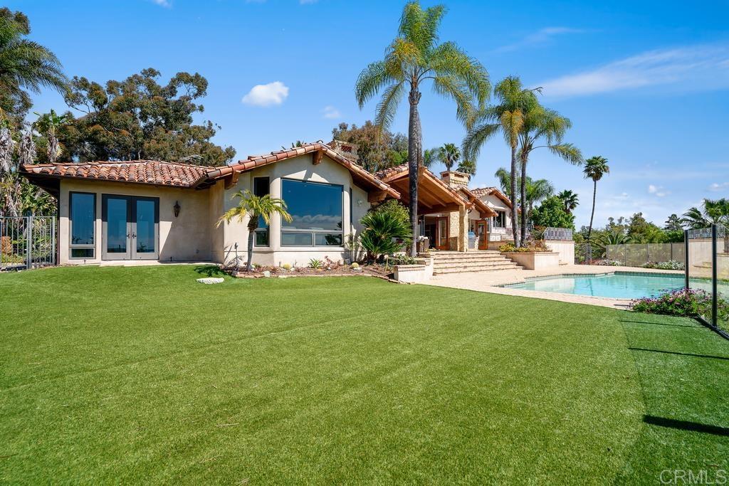 Home’s rear exterior with a broad lawn, palm trees, and swimming pool.