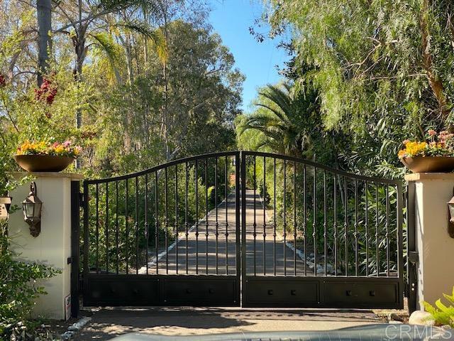 Wrought-iron entrance gate opening onto a stone path through lush landscaping.