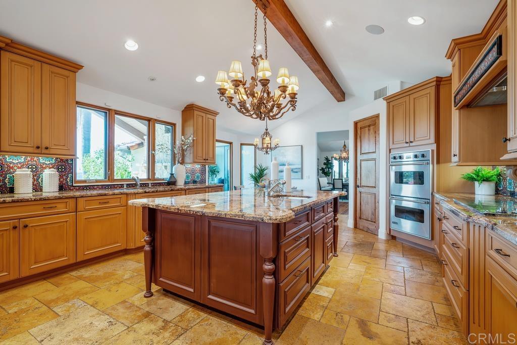 Kitchen with a large granite island, warm wood cabinetry, patterned tile backsplash, and double wall ovens.