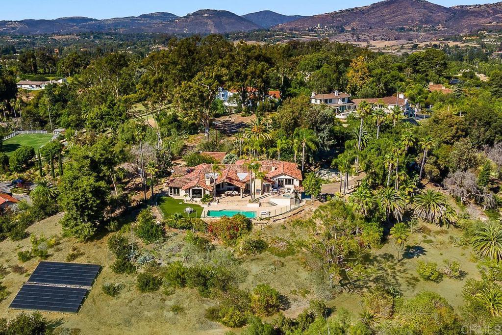 Aerial view of a tiled-roof estate with a pool, solar panels, and mountain views.