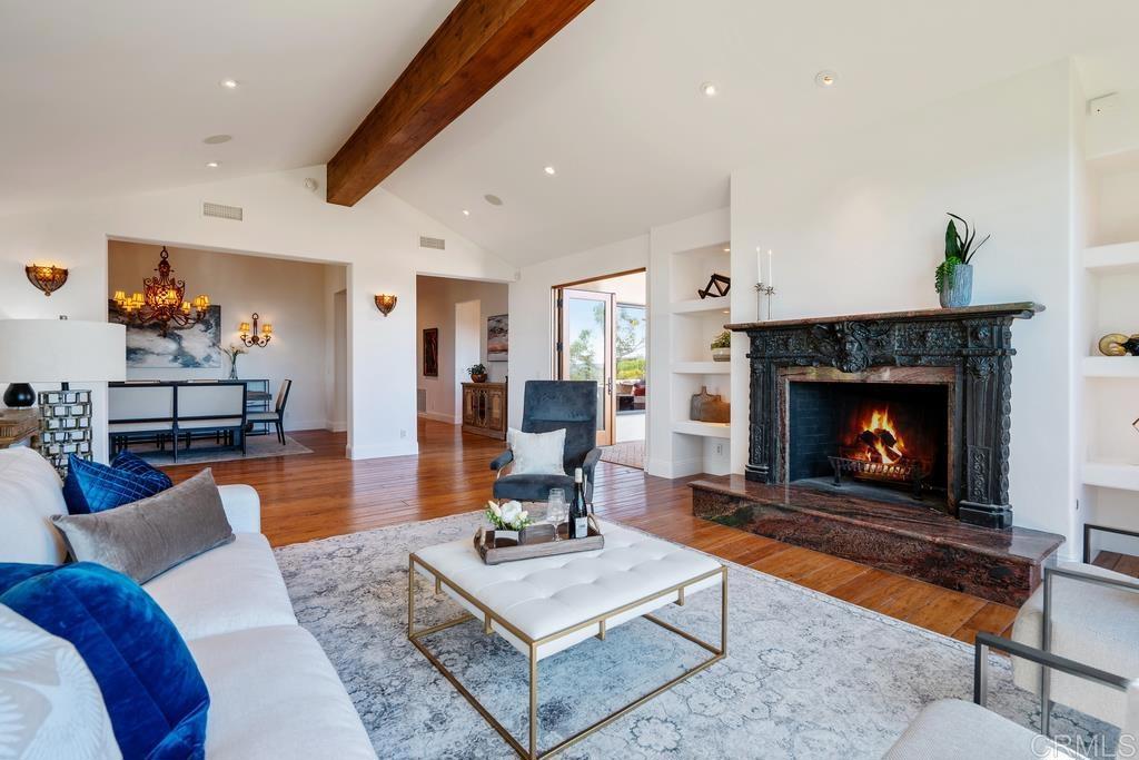Living room with an ornate black fireplace, exposed wood beam, and adjoining dining area.