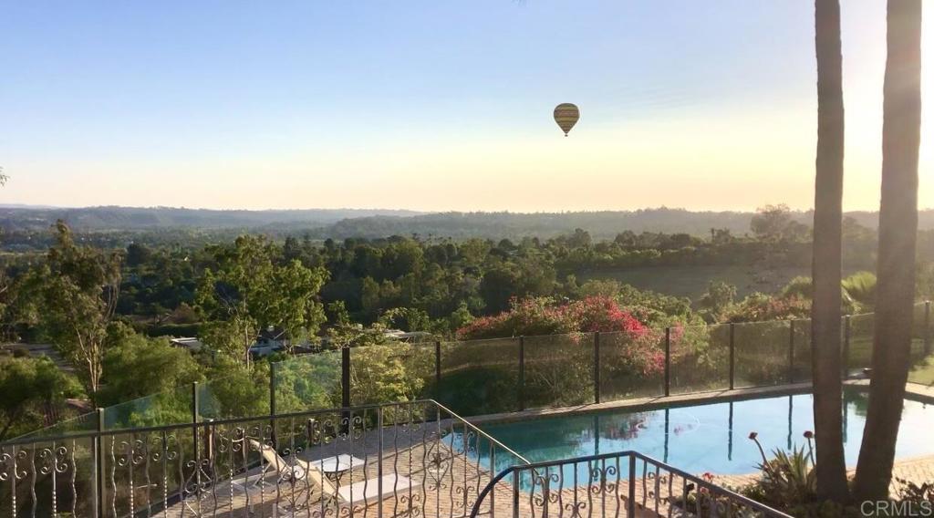 Pool terrace overlooking green hills at golden hour, with a hot-air balloon in the distance.