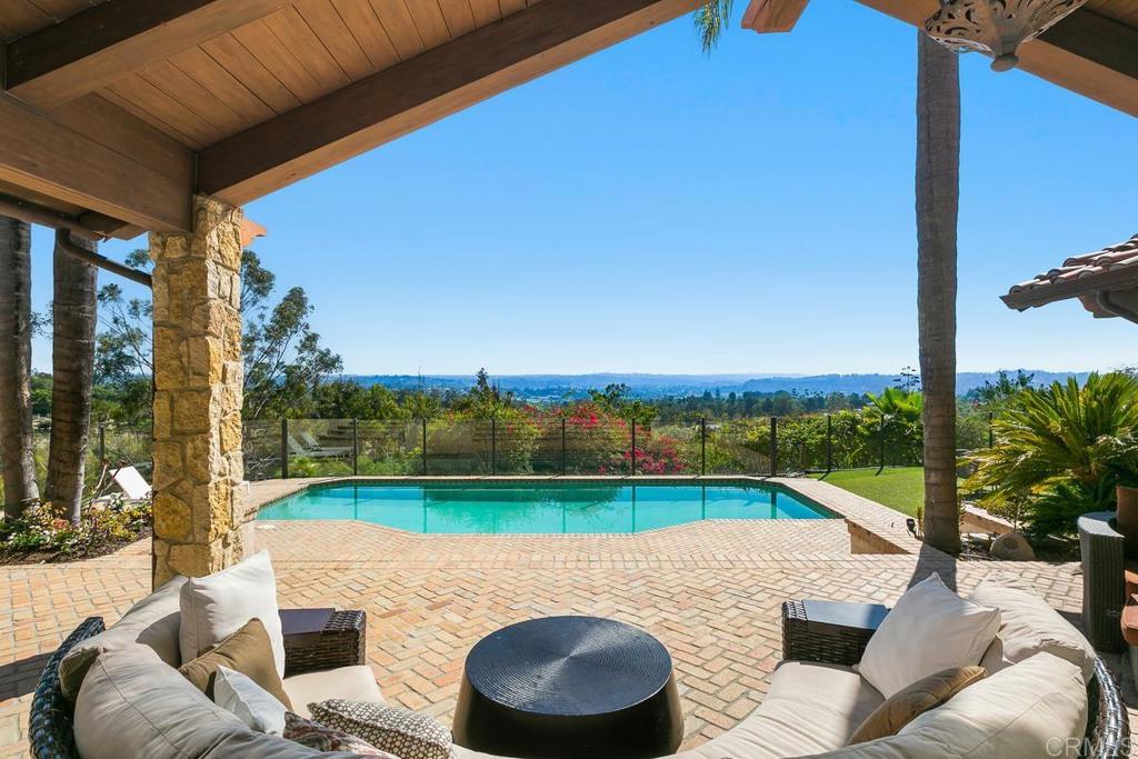 Covered patio seating overlooks a swimming pool and distant hills.
