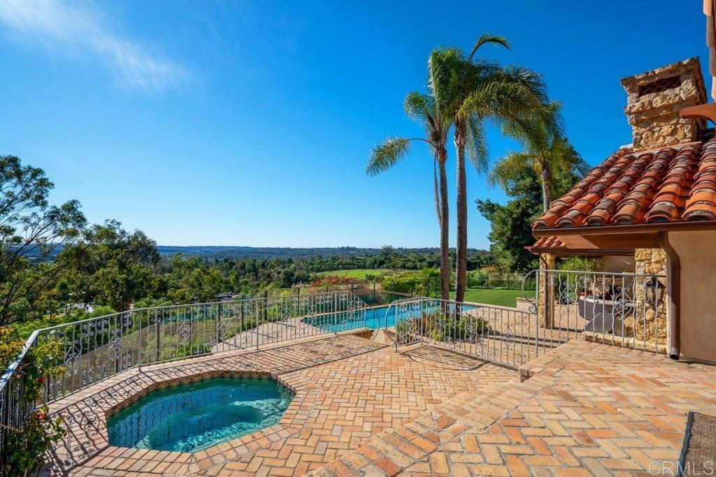 Terrace with two pools, brick paving, palm trees, and countryside views beside a Spanish-style home.