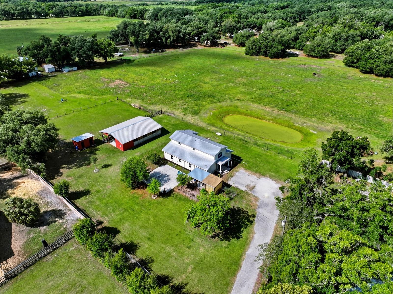 Aerial view of a white house and red outbuilding beside fenced pasture and a small pond.