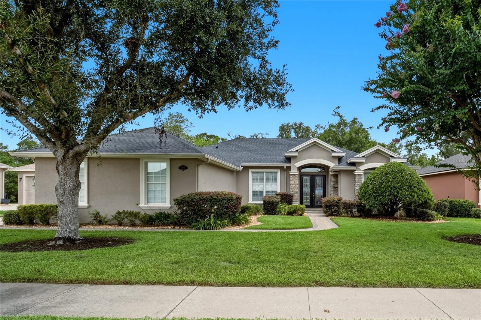 Beige single-story home with stone entry accents, dark double doors, and a broad green lawn.