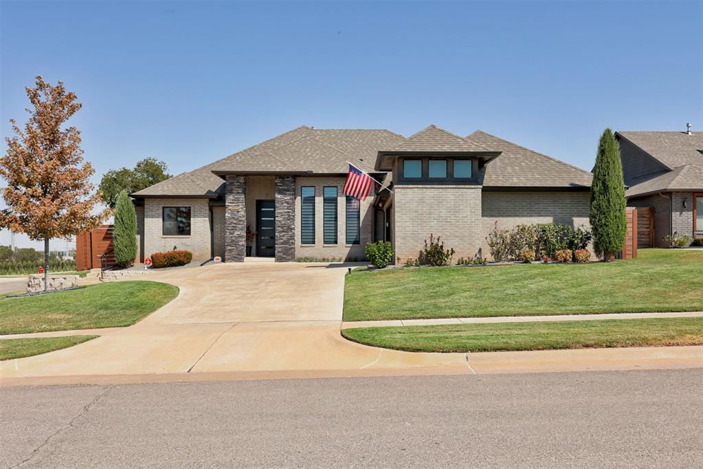 Single-story brick home with a broad driveway, landscaped lawn, and American flag by the entrance.