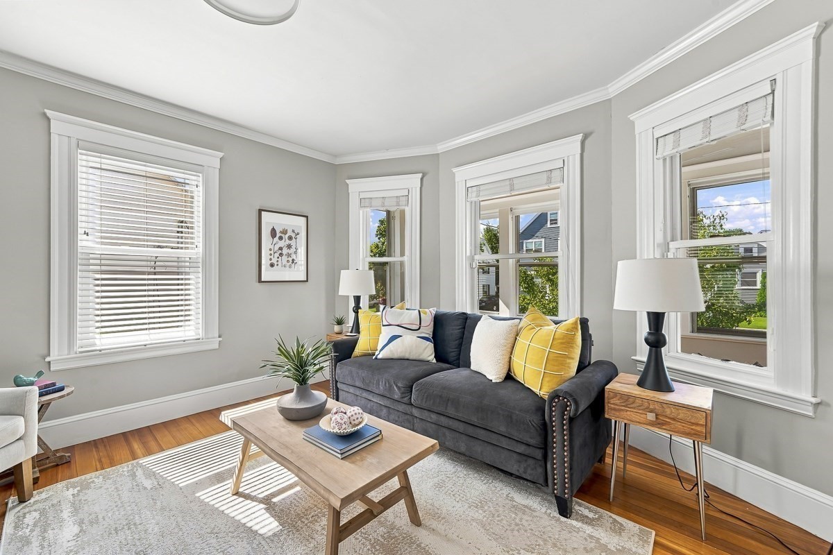 Living room with a dark gray sofa, yellow pillows, hardwood floors, and large white-trimmed windows.