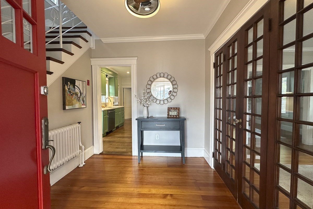 Entry hall with hardwood floors, red front door, staircase, and dark wood-framed glass doors.