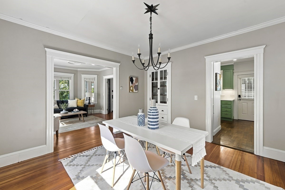 Dining room with a white table, black chandelier, hardwood floors, and views into the living room and green-accented kitchen.