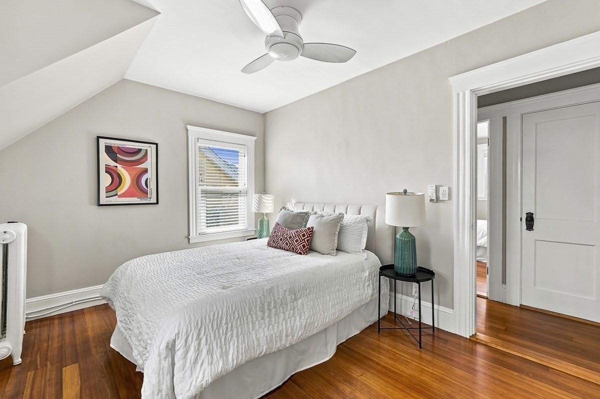 Bedroom with a white bed, hardwood floors, and a ceiling fan beneath a sloped ceiling.