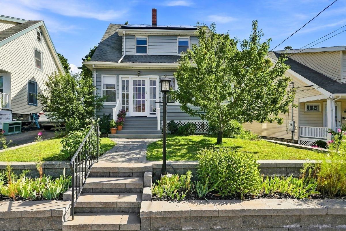 Gray two-story house with rooftop solar panels, landscaped front yard, and stone entry steps.
