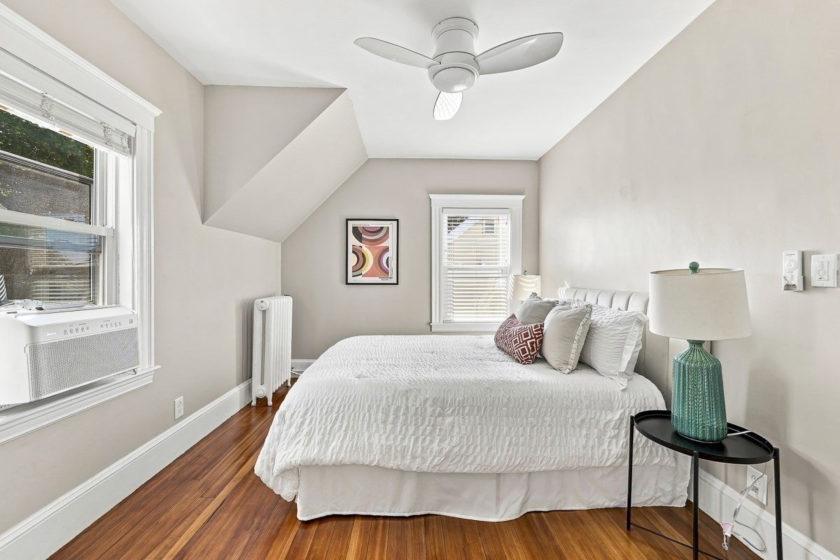 Attic bedroom with a white bed, sloped ceiling, and polished hardwood floors.