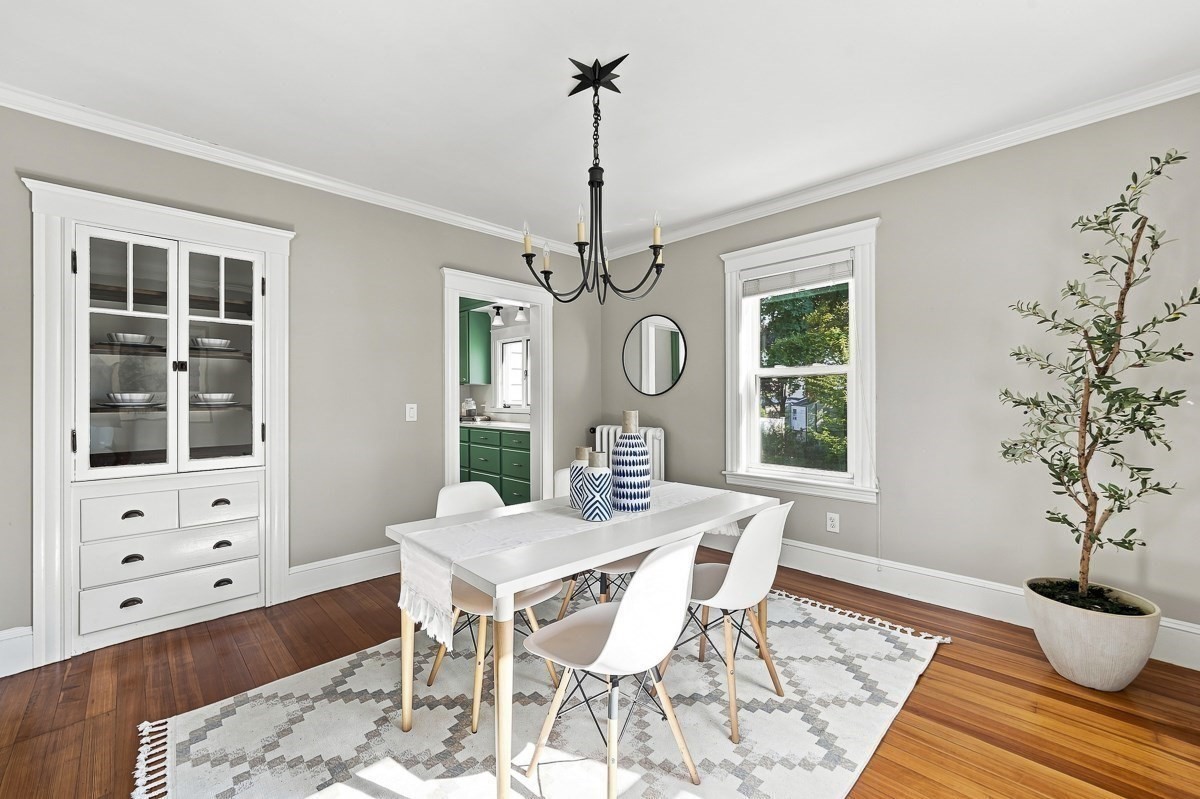 Dining room with a white table, glass-front china cabinet, hardwood floors, and doorway to a green kitchen.