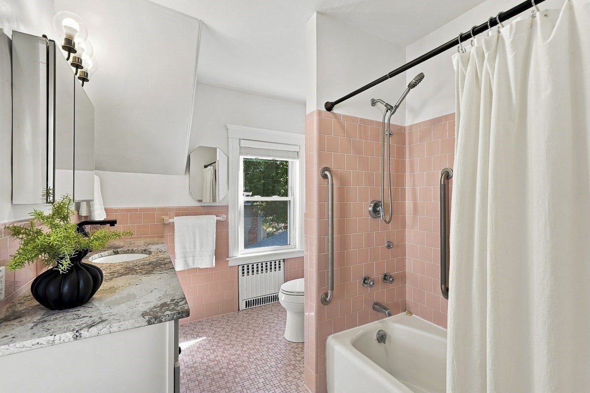 Bathroom with pink tile, a marble-look vanity, and a tub-shower with grab bars.