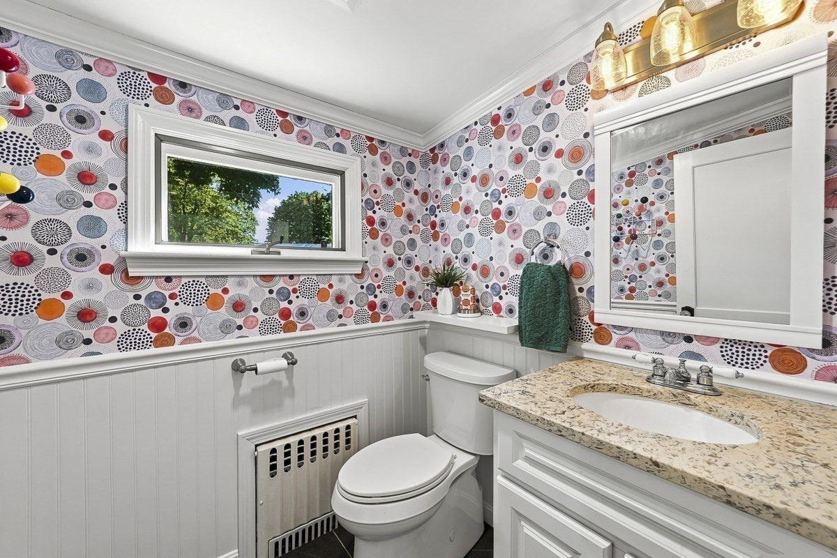 Bathroom with colorful circular wallpaper, white beadboard wainscoting, granite vanity, and a window overlooking trees.