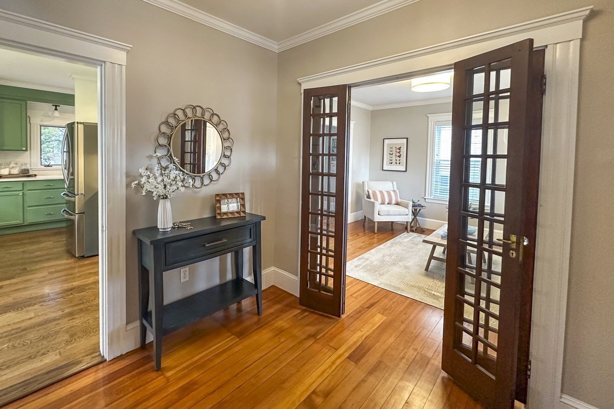Hardwood entry hall with a console table, open French doors, and a green kitchen visible to the left.