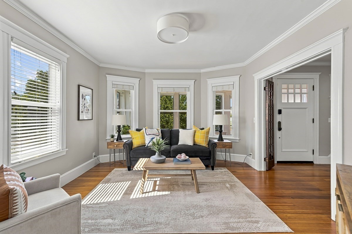 Staged living room with a dark sofa, yellow pillows, and bright windows.