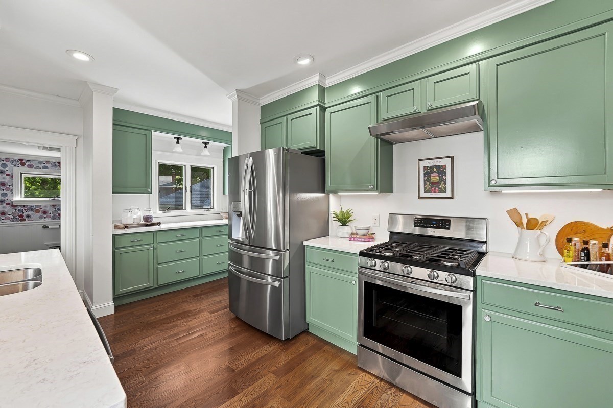 Kitchen with mint-green cabinets, stainless steel appliances, white counters, and warm wood floors.