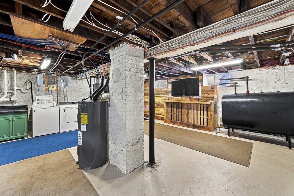 Basement laundry and utility area with exposed ceiling joists, washer and dryer, and a wooden counter with TV.