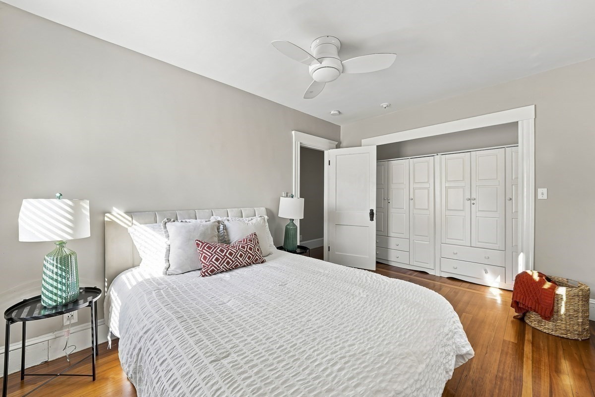 Bedroom with a white bed, built-in closets, hardwood floors, and a ceiling fan.