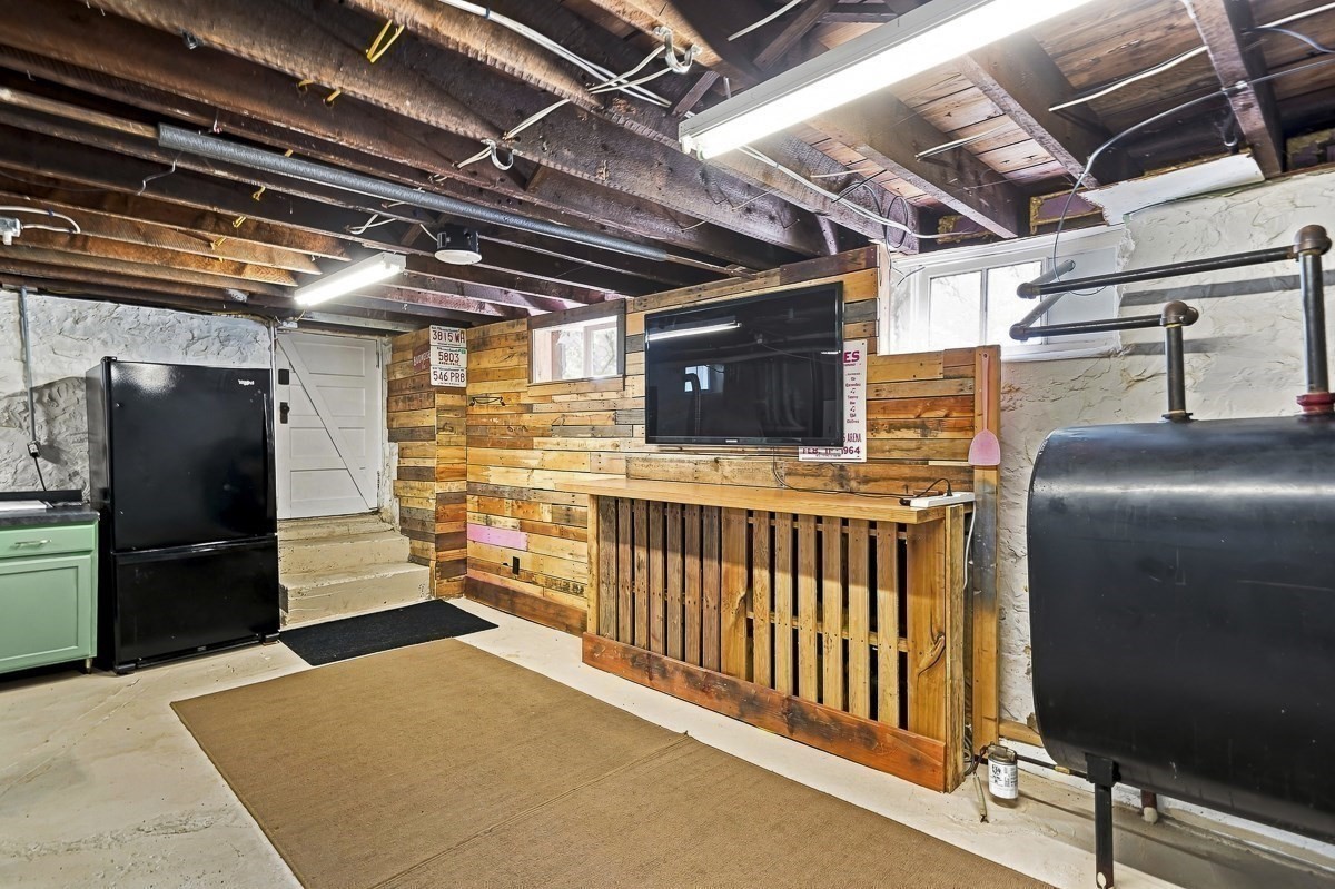 Basement recreation area with a wood-plank TV wall, exposed joists, refrigerator, and large heating tank.