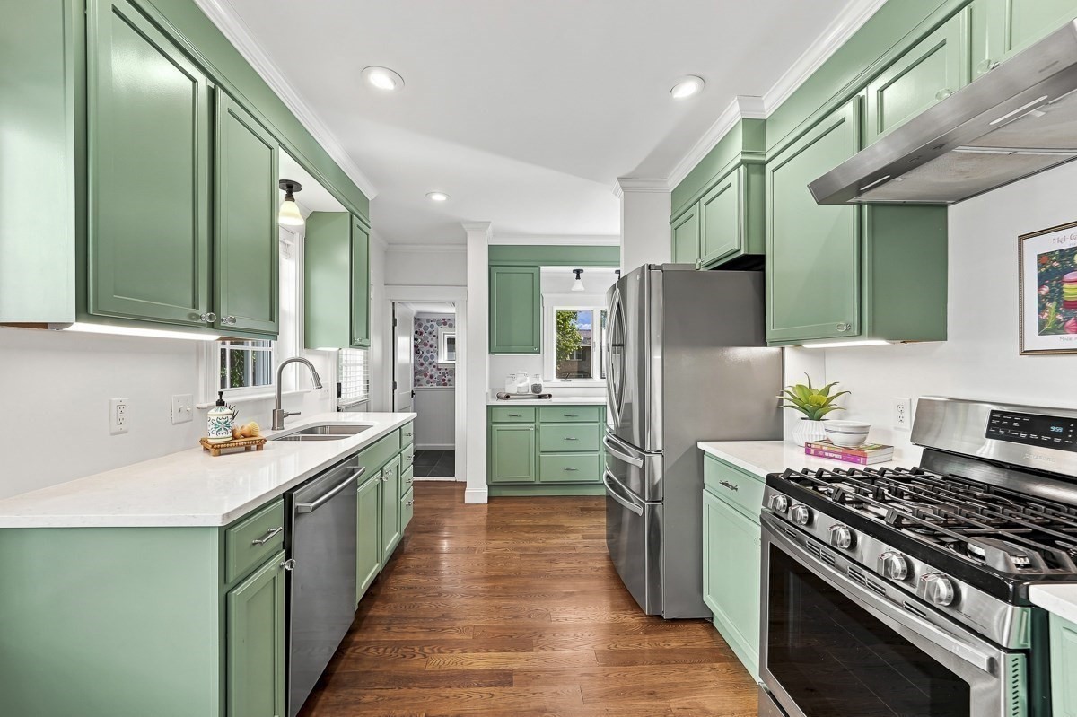 Kitchen with sage-green cabinets, white countertops, stainless steel appliances, and hardwood floors.