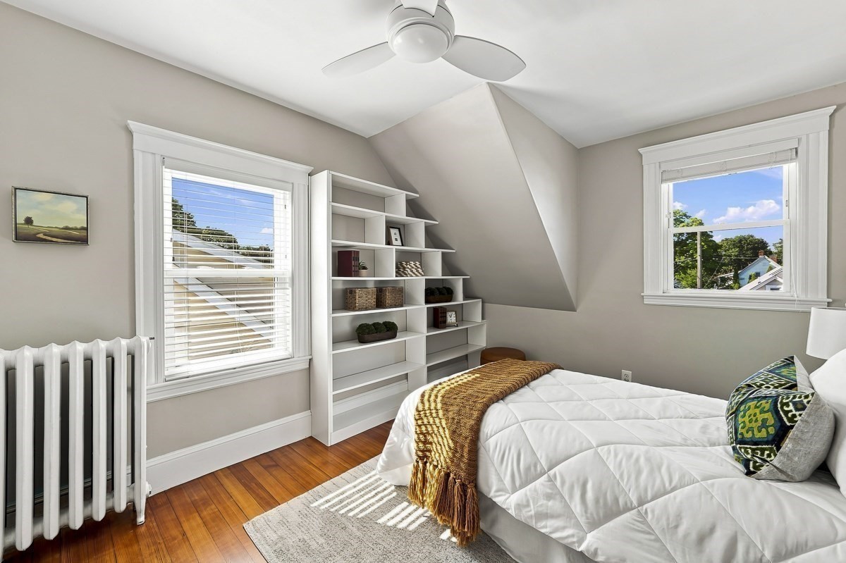 Attic bedroom with built-in stepped shelving, a white bed, ceiling fan, and hardwood floors.