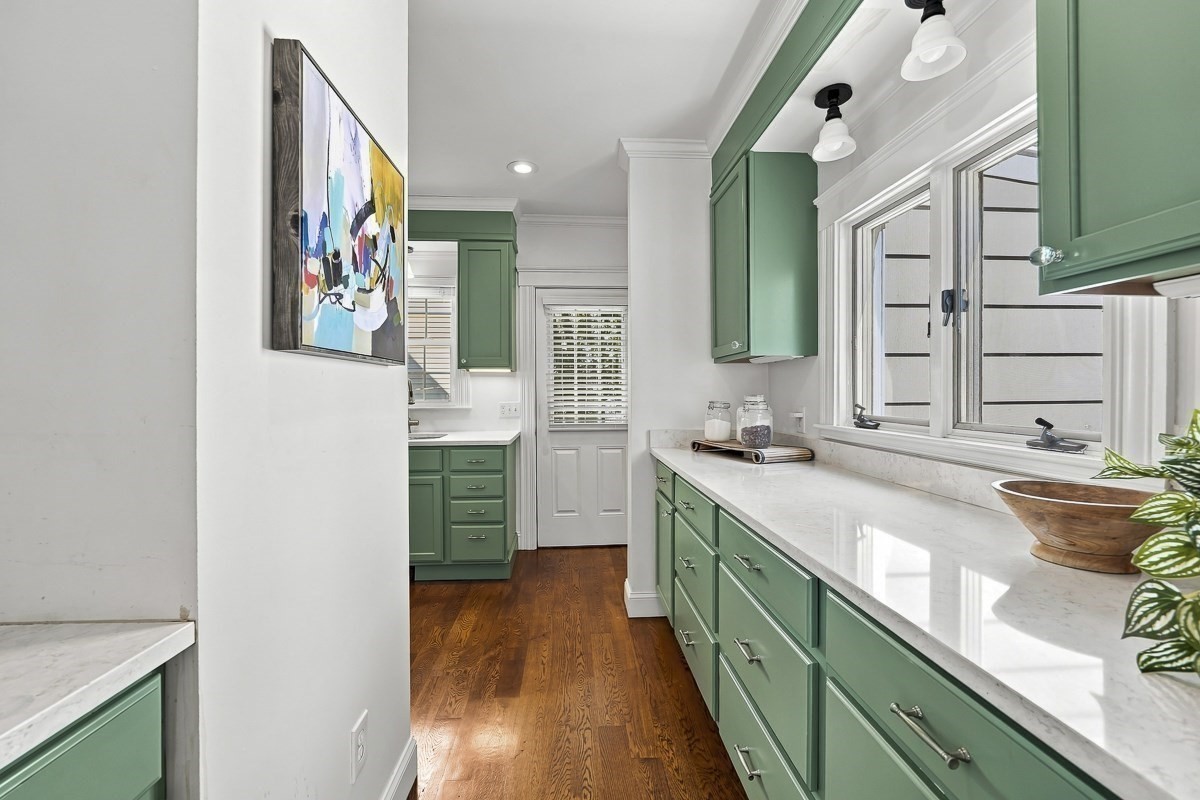 Kitchen with sage-green cabinets, white countertops, and dark wood floors.