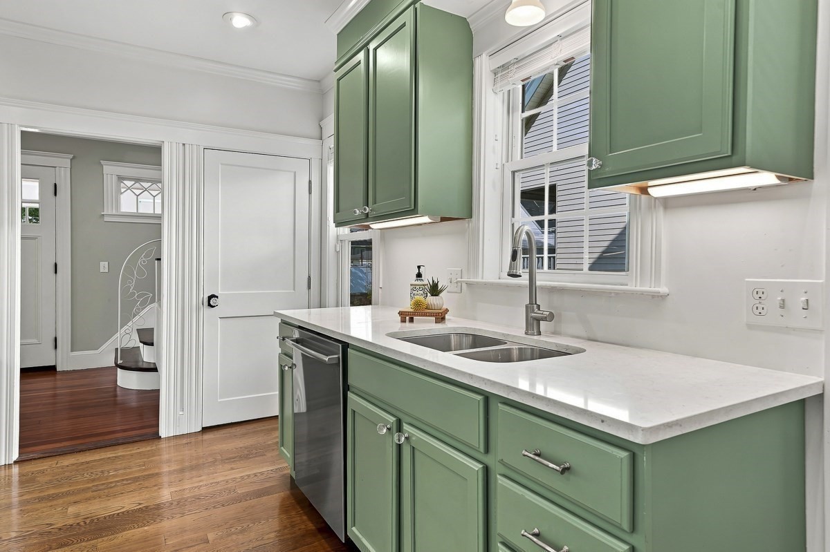 Kitchen with sage-green cabinets, white counters, and a double-basin sink beneath a window.