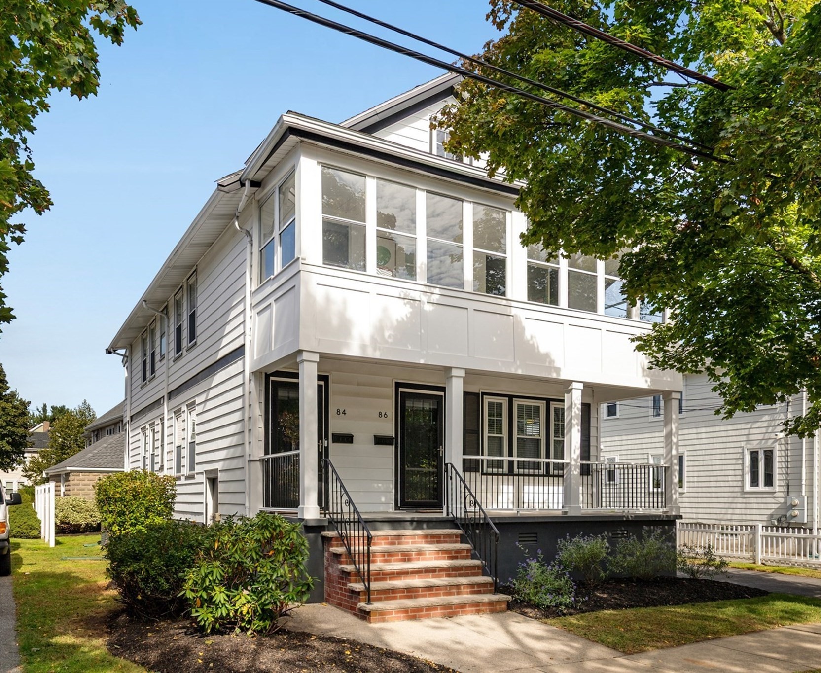 Gray two-story home with a glass-enclosed upper porch and brick front steps.