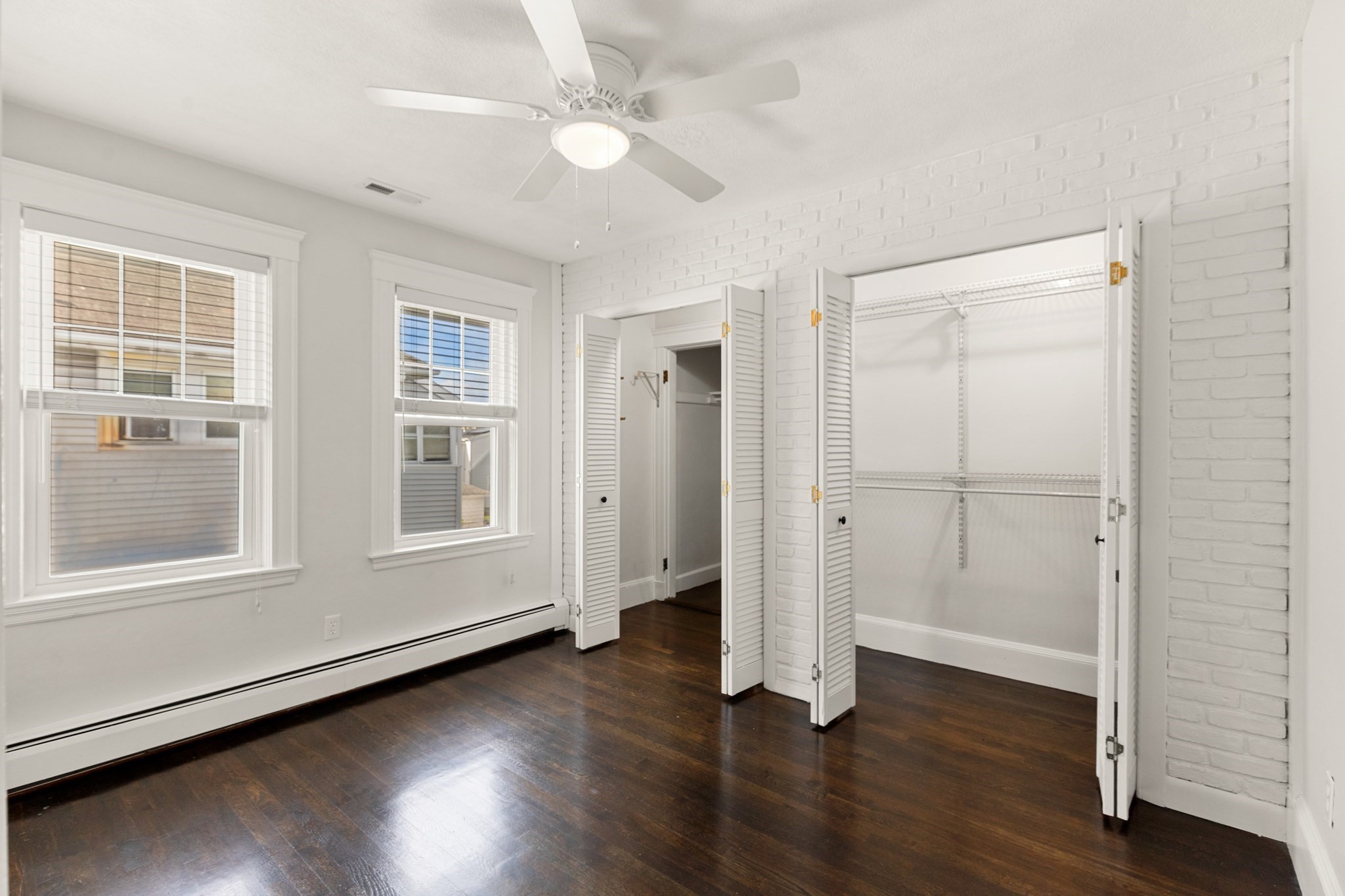 Empty bedroom with dark hardwood floors, two windows, and an open closet with wire shelving.