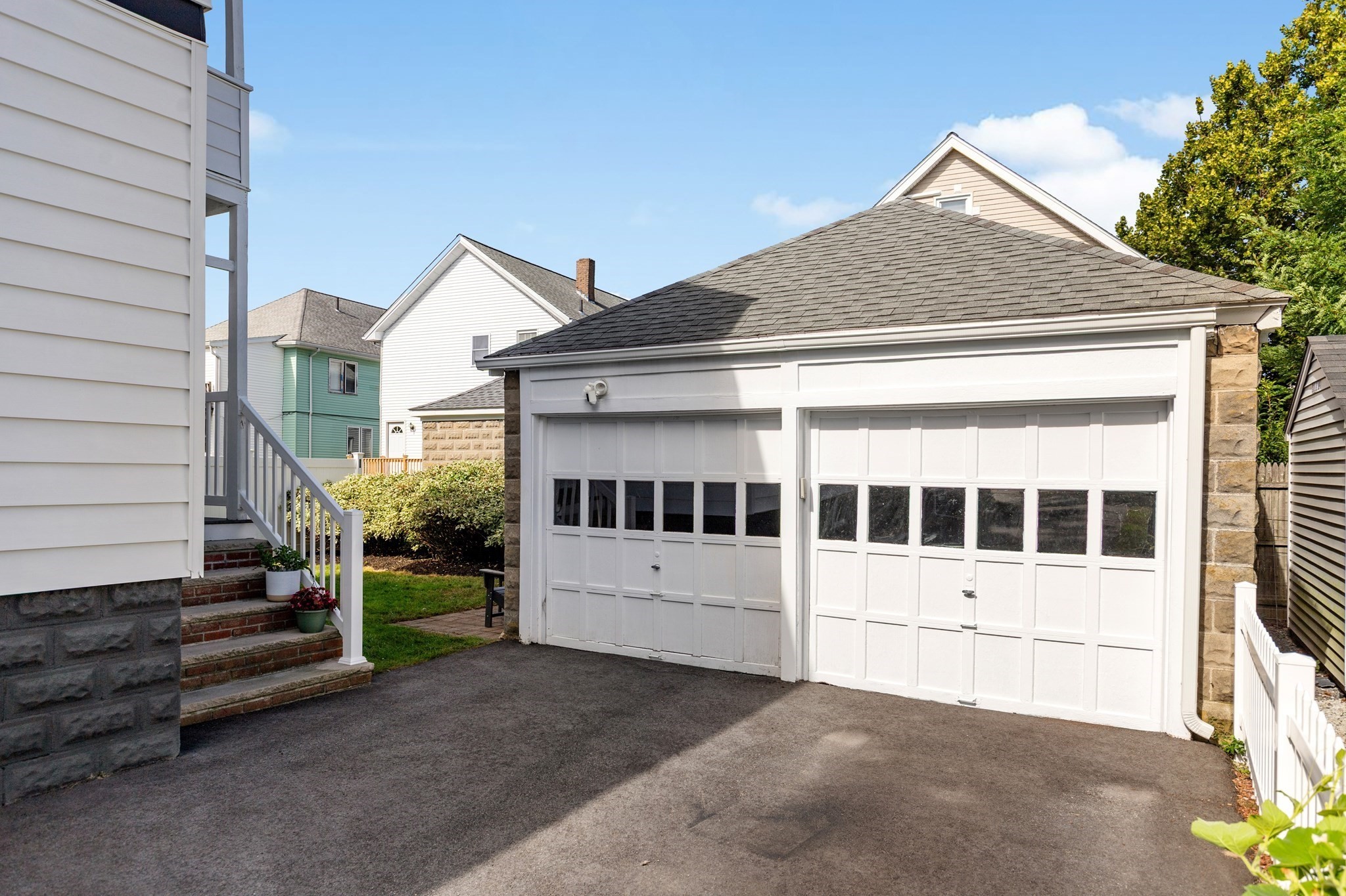White double garage with paneled doors beside an asphalt driveway and house steps.