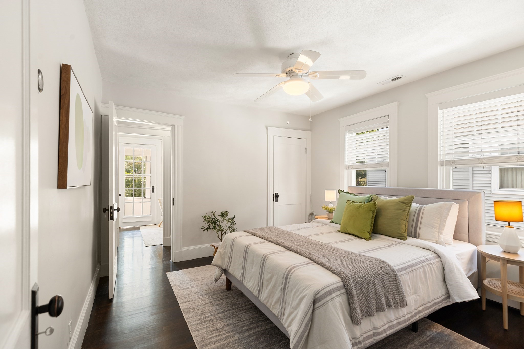 Staged bedroom with a large bed, green pillows, dark hardwood floors, and windows with blinds.