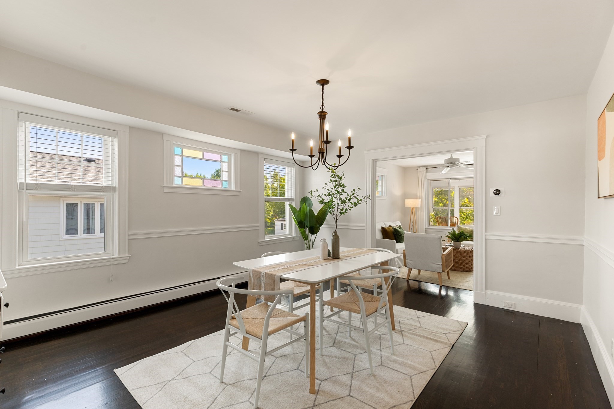 Staged dining room with a white table, chandelier, colored-glass window, and doorway to the living room.