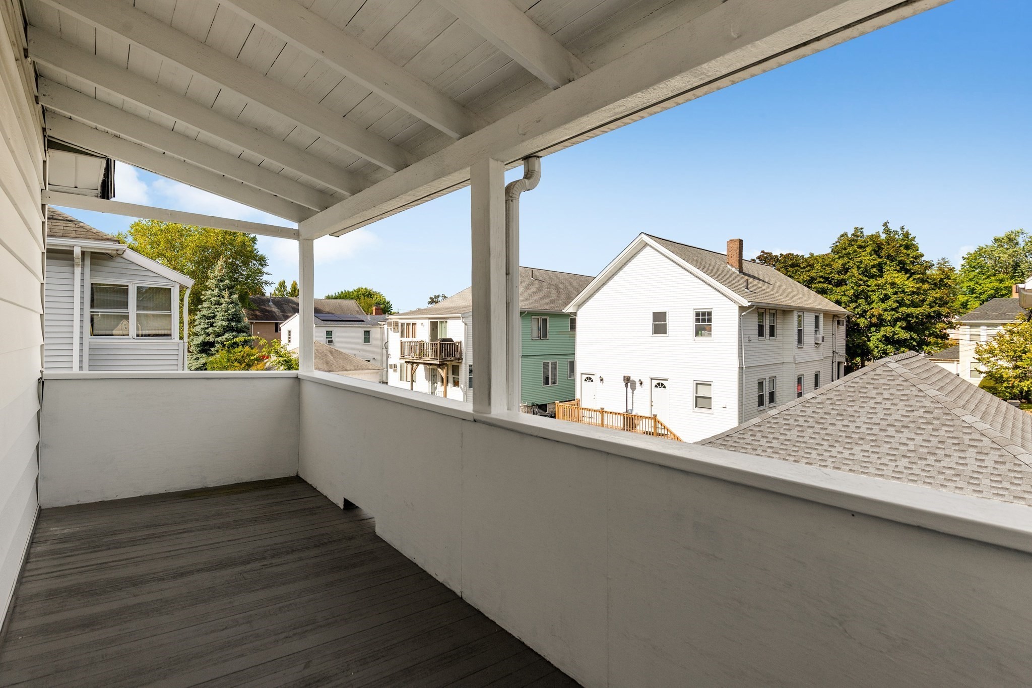 Covered porch with white railings overlooking neighboring homes and leafy trees.